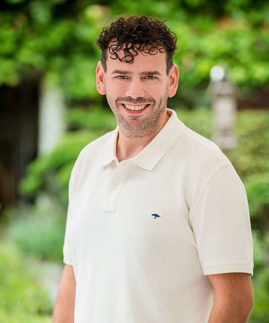 white man with dark hair smiling with white polo shirt