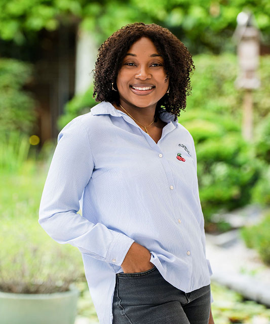 dark woman with blue shirt one hand in trouser pocket