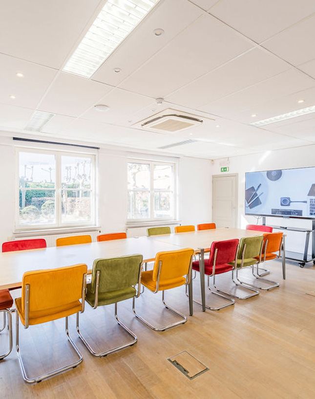 Room with long table, colorful chairs, screen